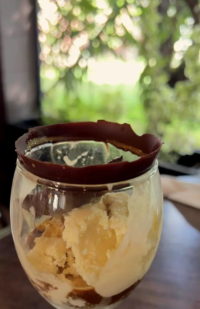 Postre en copa con borde de chocolate frente al jardín.