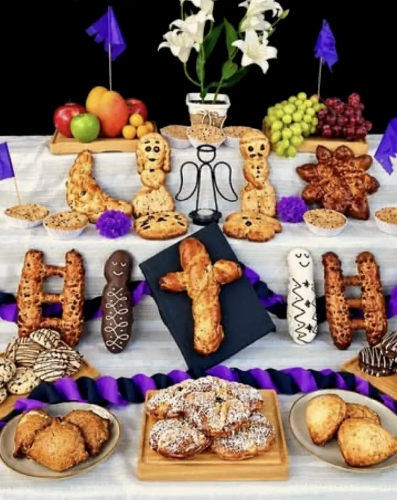 Mesa de Todos Santos con tantawawas, escaleras de pan, cruz, flores blancas y frutas.