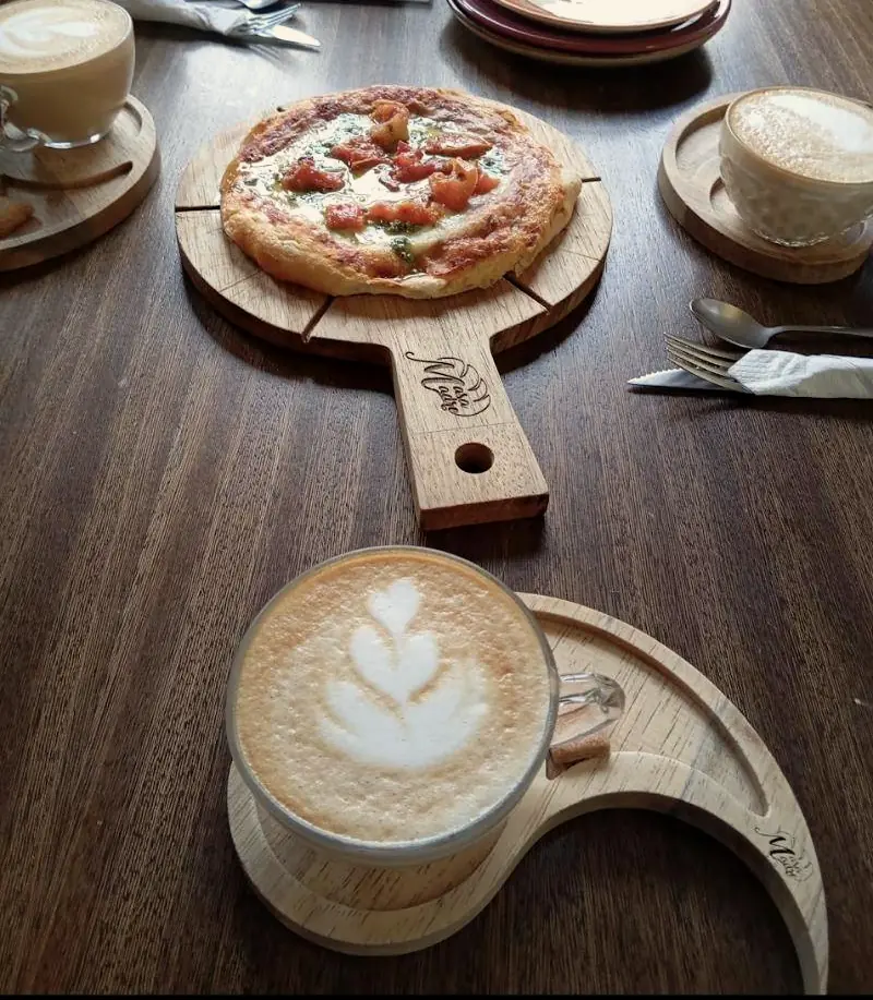 Pizzeta de masa madre sobre tabla con el logo de Masa Madre y un latte en bandeja de luna.
