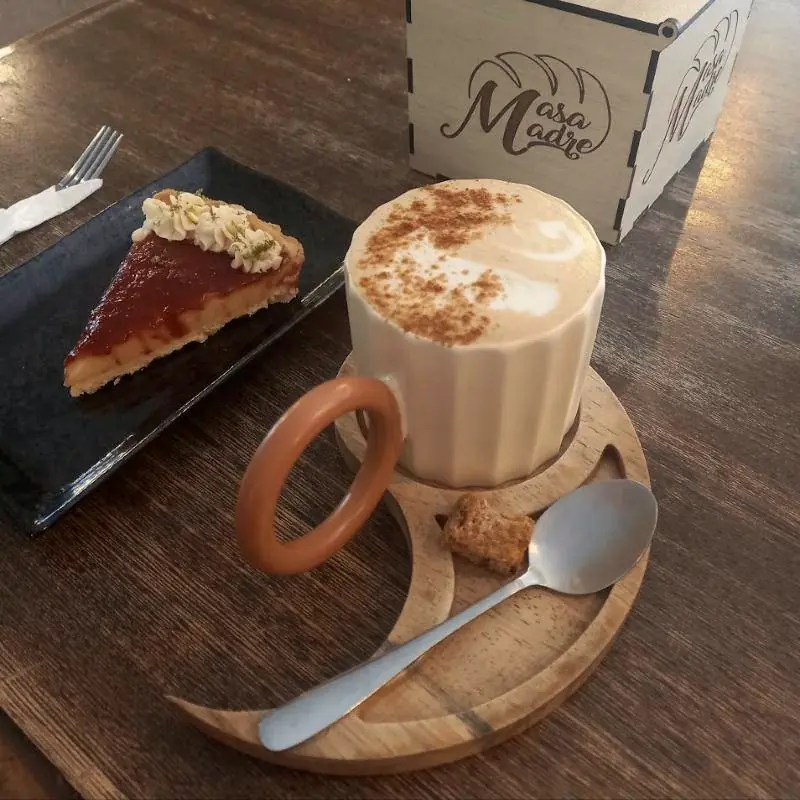 Latte con canela sobre un platillo de madera con forma de luna creciente, junto a una tarta.